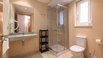 Een badkamer met een douchecabine van glas, toilet, wastafel met spiegel en raam.