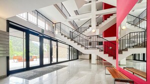 Eine großzügige Lobby mit einer modernen Treppe, großen Glasüren, die nach draußen führen, und einem polierten Boden.