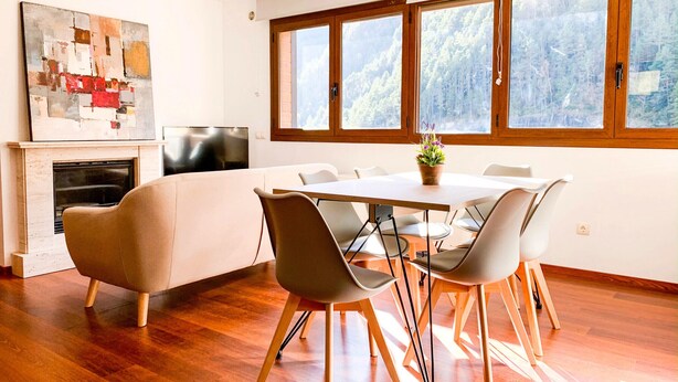 A modern dining area with a wooden table and chairs, a fireplace, and large windows offering a forest view. - Modern Apartment, 5 ppl, 2 Bedrooms, Includes Parking (Arinsal)