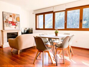 Un'area pranzo moderna con un tavolo e sedie in legno, un camino e ampie finestre con vista sulla foresta.