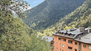 A multi-story building with a flat roof and a stone facade, surrounded by dense forest and mountains. - Modern Apartment, 5 ppl, 2 Bedrooms, Includes Parking (Arinsal)