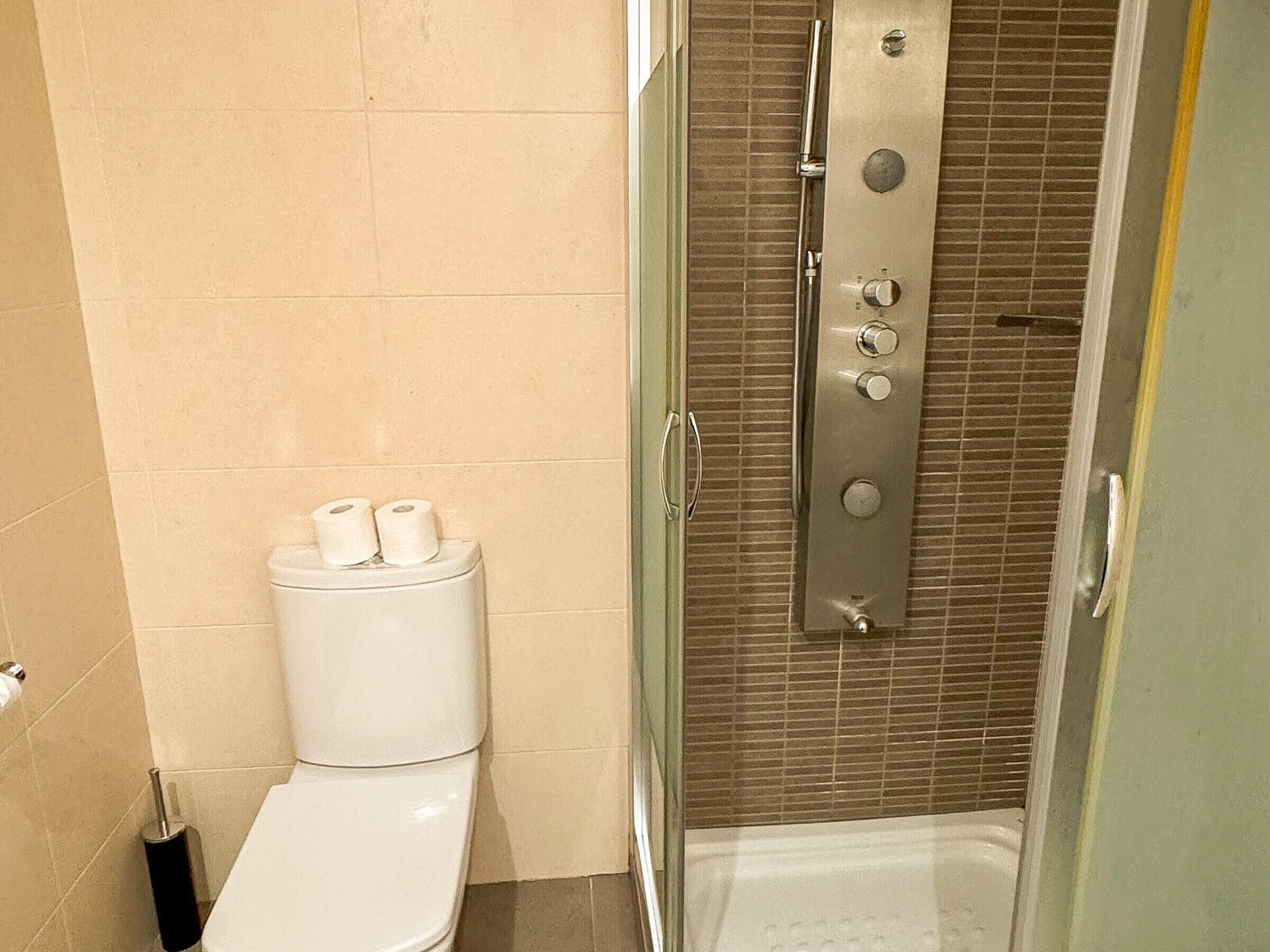 Een badkamer met toilet, douche met glazen deur en een toiletrolhouder.