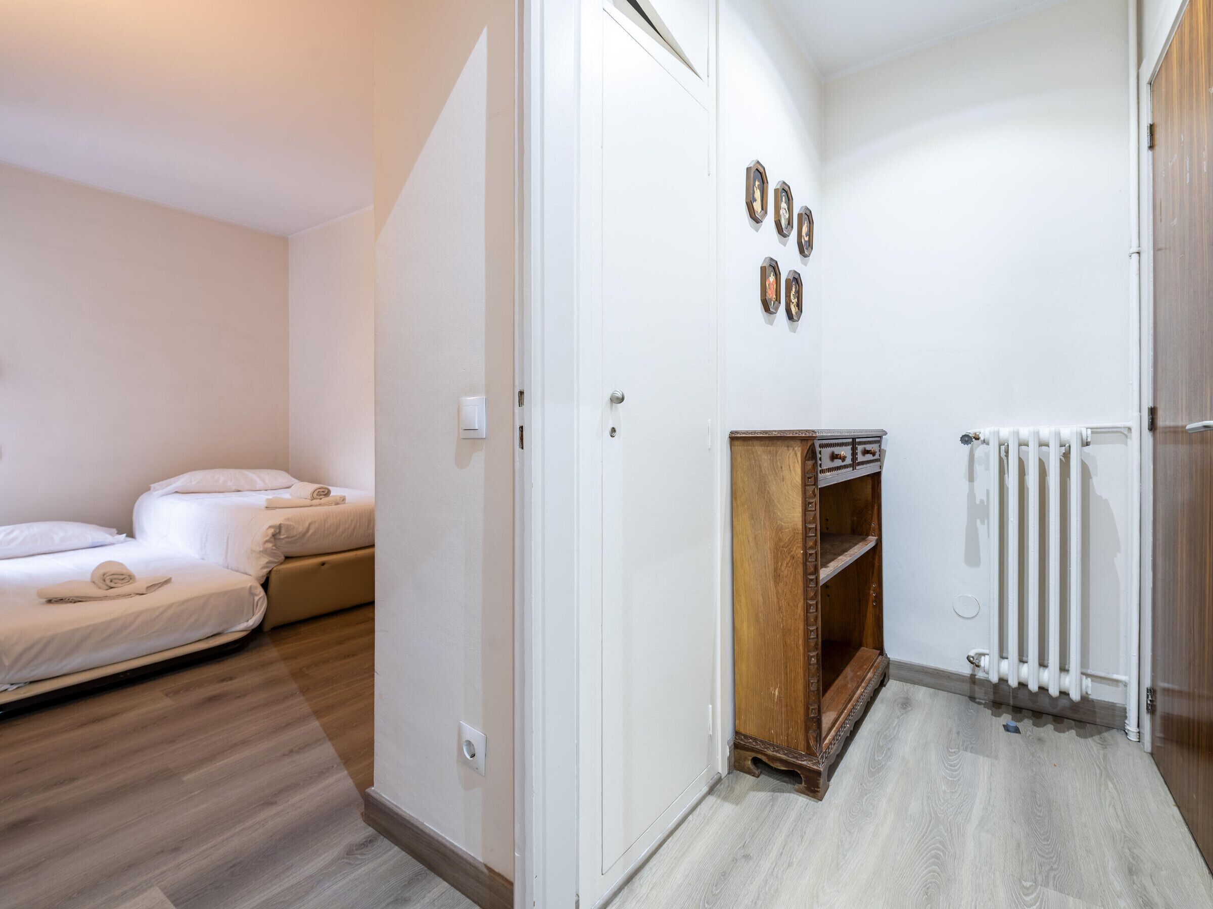 A hotel room with two beds, a wooden cabinet, a radiator, and wall-mounted artwork.