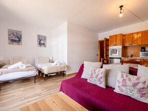 A cozy room with two beds, a wooden floor, a kitchen with wooden cabinets, and artwork on the walls. - Cozy Studio in El Tarter - 2 people, near slopes (El Tarter)