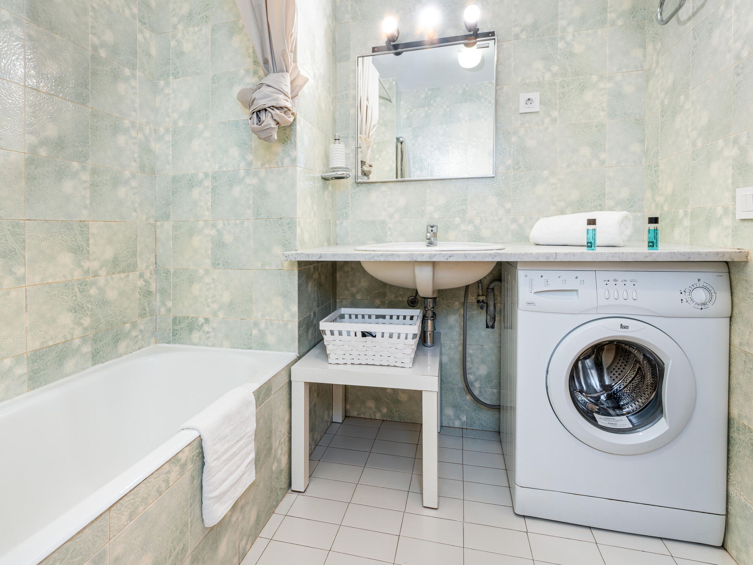 Une salle de bain équipée d’une baignoire, d’un lavabo, d’un miroir, d’une machine à laver et d’un porte-serviettes.