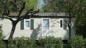 A single-story house with a white exterior, green shutters, and a small porch area. - Cozy mobile home 2 bedrooms 6 people in Montblanc (Montblanc)