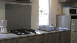 A kitchen with a gas stove, a microwave, and a sink. - Cozy mobile home 2 bedrooms 6 people in Montblanc (Montblanc)