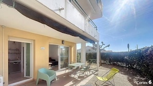 Un edificio de dos pisos con un balcón, un comedor con mesa y sillas, y una pequeña cocina.