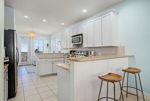 A modern kitchen with white cabinets, a microwave, and a central island with stools.