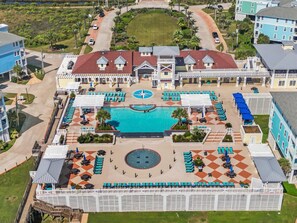 An aerial view of a resort with a central pool, multiple lounge areas, and a large building with a red roof.