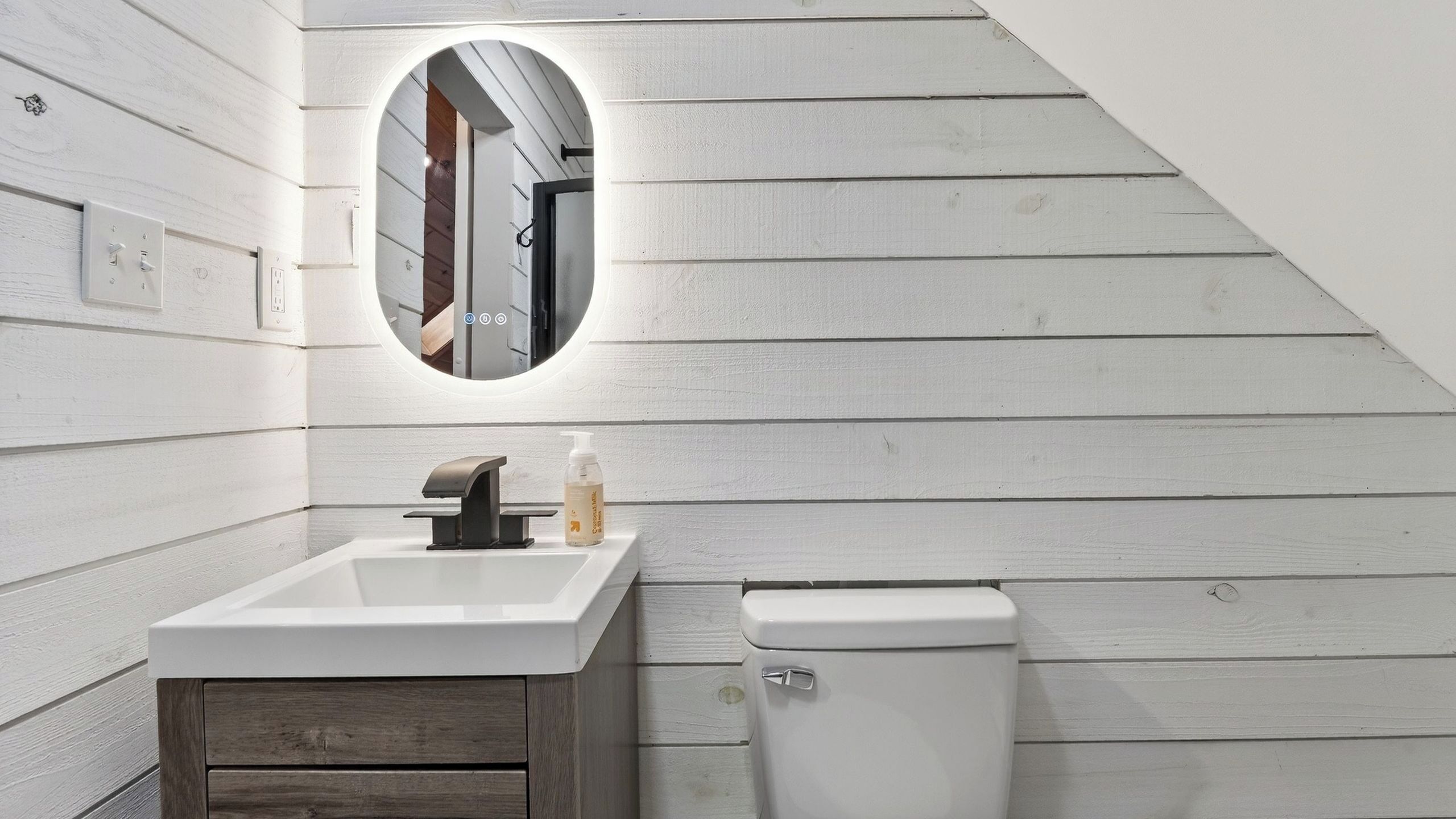 Un baño con lavamanos blanco, espejo, inodoro y paneles de madera en las paredes.