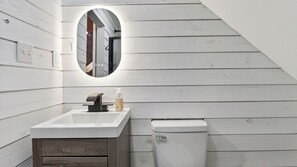 A bathroom with a white sink, a mirror, a toilet, and wooden paneling on the walls. - Evergreen Lodge by Avantstay Poconos Lake Cabin + Fireplace + Large Deck + Near Jack Frost & Kalahari (Pocono Lake)