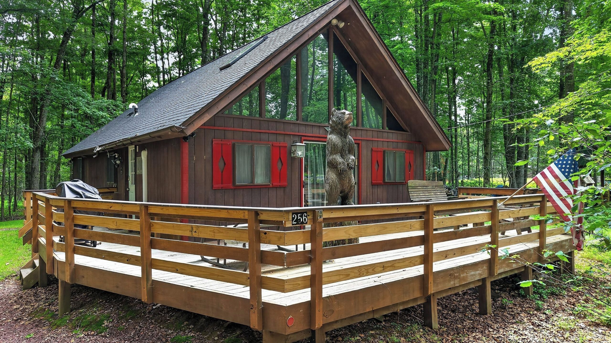 A cabin with a wooden deck, a bear statue, and an American flag.