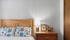 A bedroom with a wooden headboard, a bed with patterned pillows, a bedside table with a lamp, and a framed picture. - Evergreen Lodge by Avantstay Poconos Lake Cabin + Fireplace + Large Deck + Near Jack Frost & Kalahari (Pocono Lake)