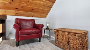 A red leather armchair, a small round table with a lamp, and a wicker storage box in a room with wooden ceiling and white walls. - Evergreen Lodge by Avantstay Poconos Lake Cabin + Fireplace + Large Deck + Near Jack Frost & Kalahari (Pocono Lake)