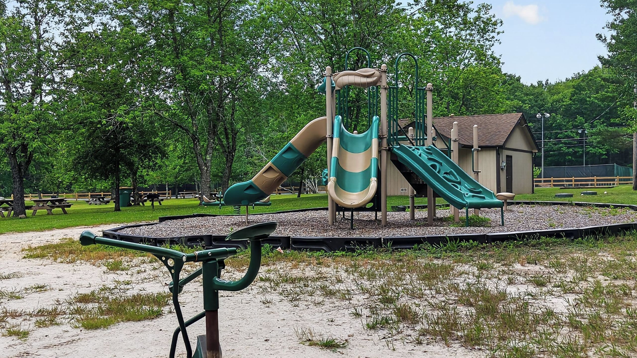 A playground with slides and swings, surrounded by trees and a picnic area.