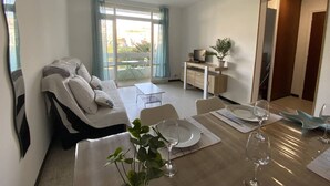 Una sala de estar moderna con un sofá, una mesa de comedor para dos personas y un balcón con vistas.