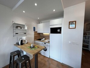 A compact kitchen with a wooden table, two stools, a washing machine, and a microwave. - Charming apartment with parking - 4 guests (Port Grimaud)