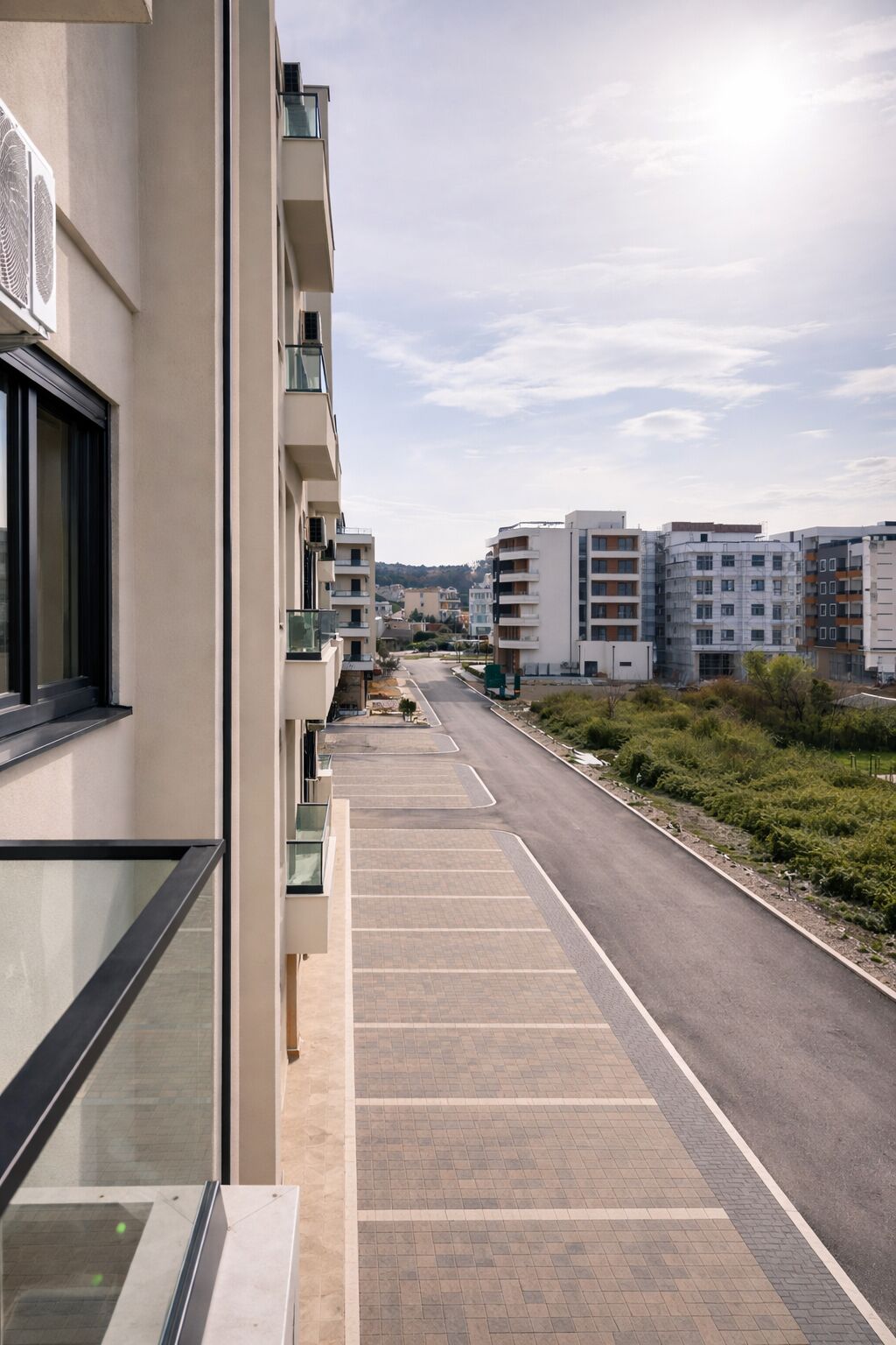 A residential building with balconies, a paved walkway, and a road in the background.