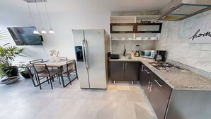 A modern kitchen with a built-in refrigerator, a dining area with a table and chairs, and a countertop with a stove. - Océano Aria, Entire Lodging: Condominium in Bucerias, Mexico (Nuevo Vallarta)