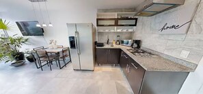 Eine moderne Küche mit Einbaukühlschrank, einem Essbereich inklusive Tisch und Stühlen sowie einer Arbeitsplatte mit Herd.