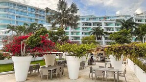 An outdoor patio area with tables and chairs, surrounded by large potted plants and palm trees. - Océano Aria, Entire Lodging: Condominium in Bucerias, Mexico (Nuevo Vallarta)