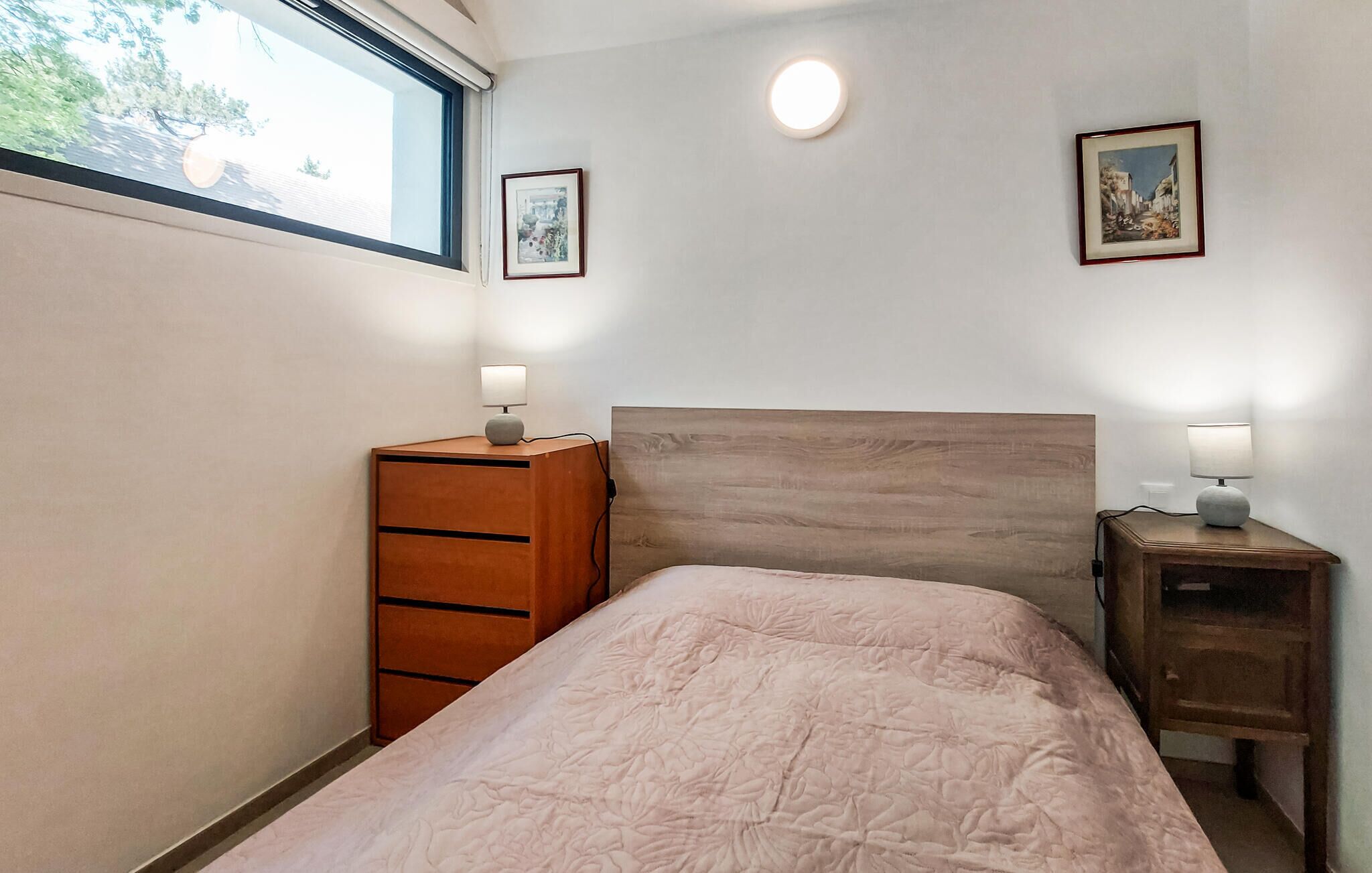 Un dormitorio con cama, cómoda, mesita de noche y dos marcos con cuadros colgados en la pared.