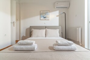 Een keurig opgemaakt slaapkamer met een bed, kussens, een radiator en een aan de muur bevestigde airconditioner.