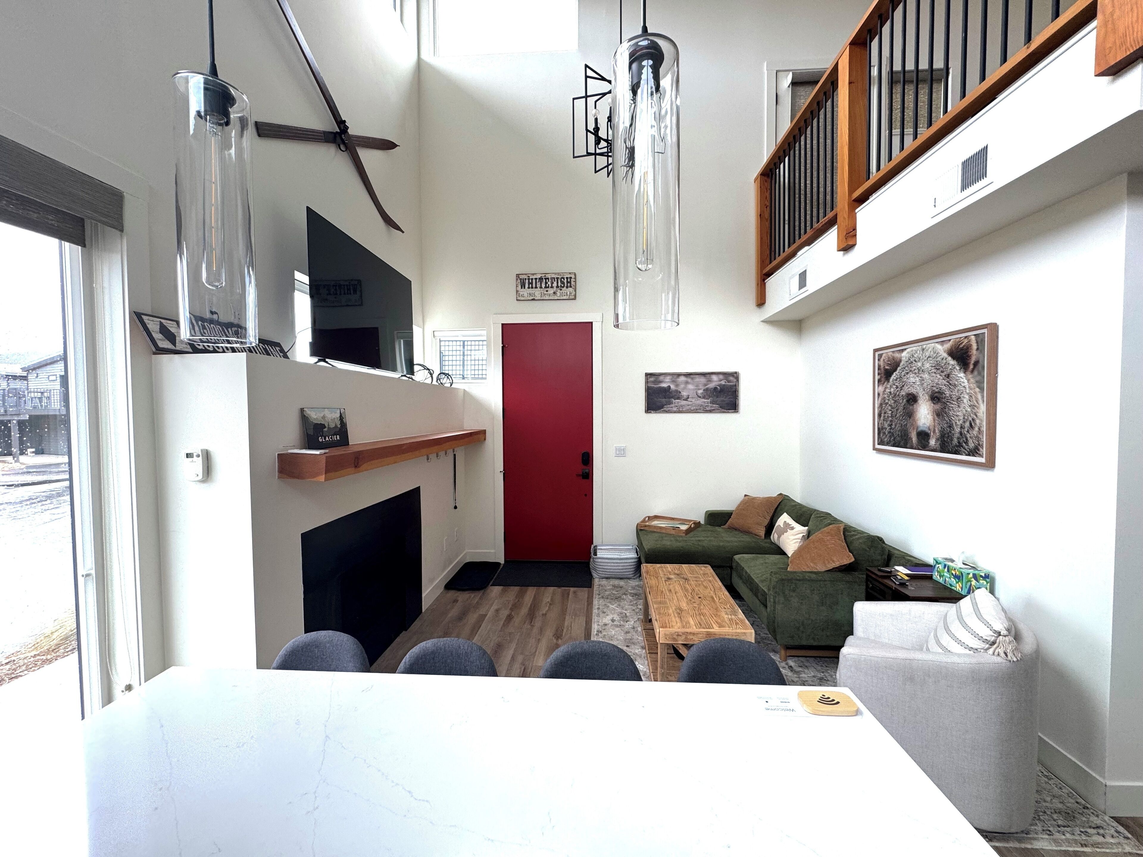 Una sala de estar moderna con chimenea, un sofá verde, una mesa de comedor con sillas y una puerta roja.