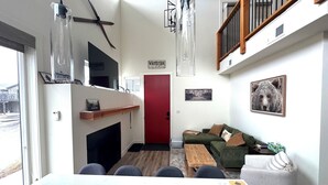 Ein modernes Wohnzimmer mit Kamin, einem grünen Sofa, einem Esstisch mit Stühlen und einer roten Tür.