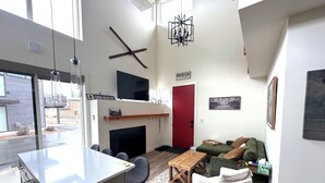 Ein modernes Wohnzimmer mit Kamin, einer roten Tür, einem Fernseher und einem Essbereich mit Bar.