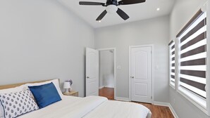 Ein Schlafzimmer mit Bett, Deckenventilator, Nachttisch, Lampe und Fenster mit Jalousien.