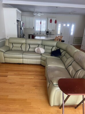A spacious living room with a large L-shaped sectional sofa, a wooden floor, and a kitchen in the background.