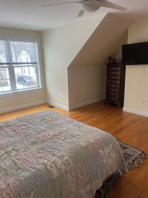 A bedroom with a large bed, a ceiling fan, a dresser, and a window with blinds.
