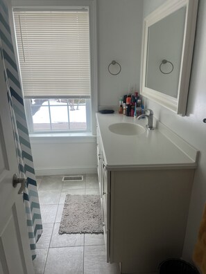 A bathroom with a window, sink, mirror, and toiletries on the counter.
