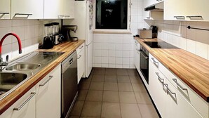 Une cuisine de taille réduite avec des meubles blancs, un lave-vaisselle, un évier, un robinet rouge et une fenêtre.