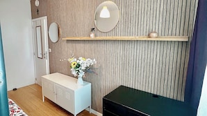 Une chambre d’hôtel moderne avec un mur lambrissé en bois, une commode blanche, un bureau noir, une chaise bleue et un lit recouvert d’une courtepointe à motifs floraux.