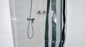 Une douche équipée d’un pommeau de douche à main et d’un robinet mural, une baignoire blanche et un rideau de douche à rayures.