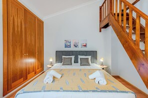 A bedroom with a large wooden wardrobe, a grey upholstered headboard, two bedside tables with lamps, and a wooden staircase. - Sao Rafael TownHouse with Pool (Albufeira)