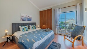 Un dormitorio con cama, mesita de noche, silla, ventana y puerta.