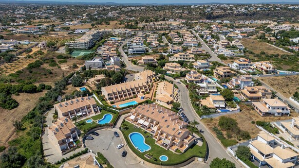 Vista aérea de una zona residencial con varios edificios de apartamentos, una piscina central y abundante vegetación.