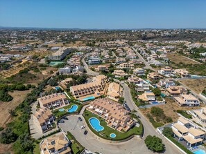 An aerial view of a residential area with multiple apartment buildings, a central swimming pool, and surrounding greenery. - Sao Rafael TownHouse with Pool (Albufeira)