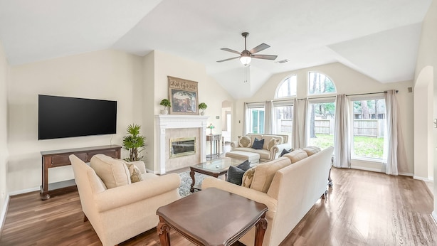 A spacious living room with a fireplace, a large TV, and a ceiling fan.