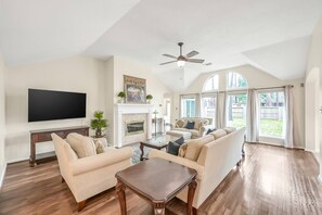 A spacious living room with a fireplace, a large TV, and a ceiling fan.