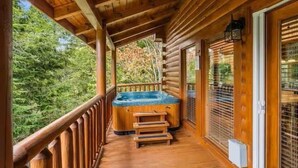 Eine Holzhütte mit Whirlpool auf einer Holzterrasse, umgeben von Bäumen.