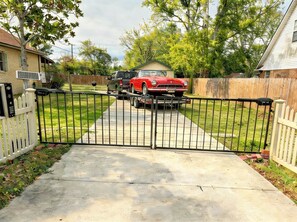 A gated driveway leading to a house with a red car parked on the street. - Peaceful & Close to Coliseum and Beach (D'Iberville)