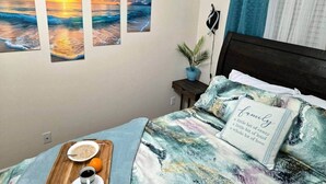 Un dormitorio con cama, mesita de noche, lámpara de pared, planta en maceta y ventana con cortinas.