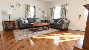 Sala de estar con dos sofás grises, una mesa de centro de madera, alfombra estampada y una puerta con interruptor de luz.