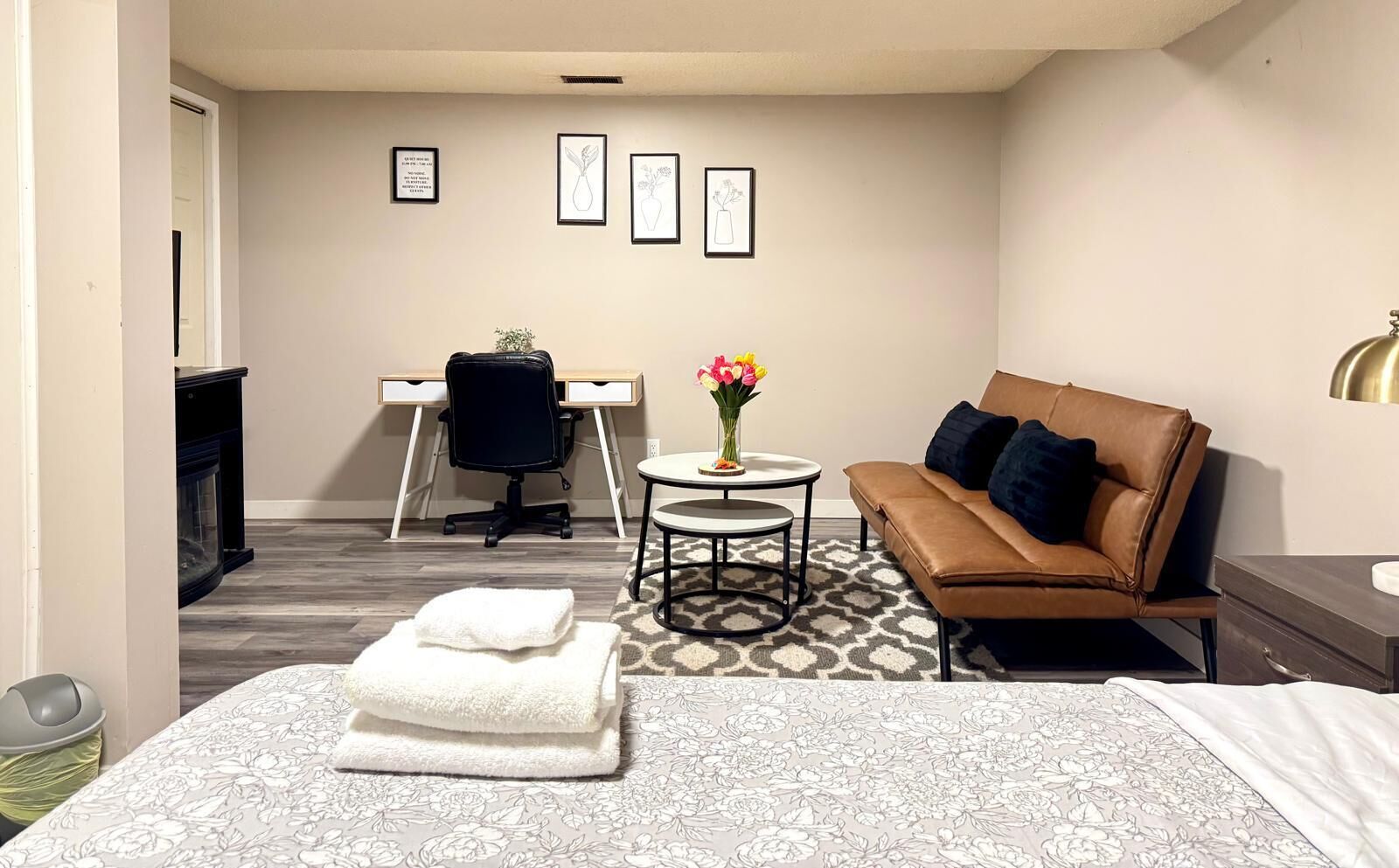 A hotel room with a bed, a sofa, a desk, a chair, a small table with a vase of flowers, and a lamp.