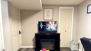 A living room with a fireplace, a television on a stand, a framed quote on the wall, and a vase of tulips. - Cozy&Private Basement Suite. Minutes from Airport, Highway, College, Restaurants (Thunder Bay)